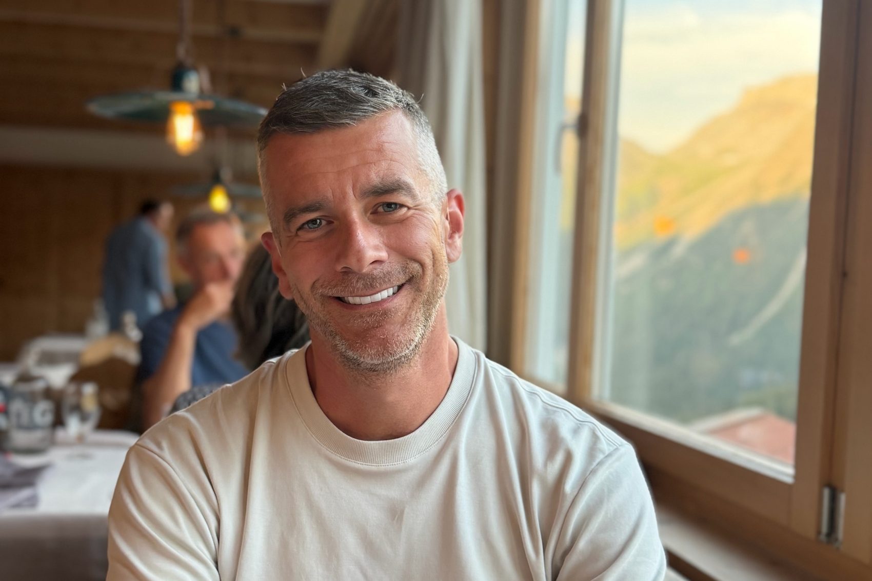 Carsten Diederich in einer Berghütte, im Fenster die Alpen
