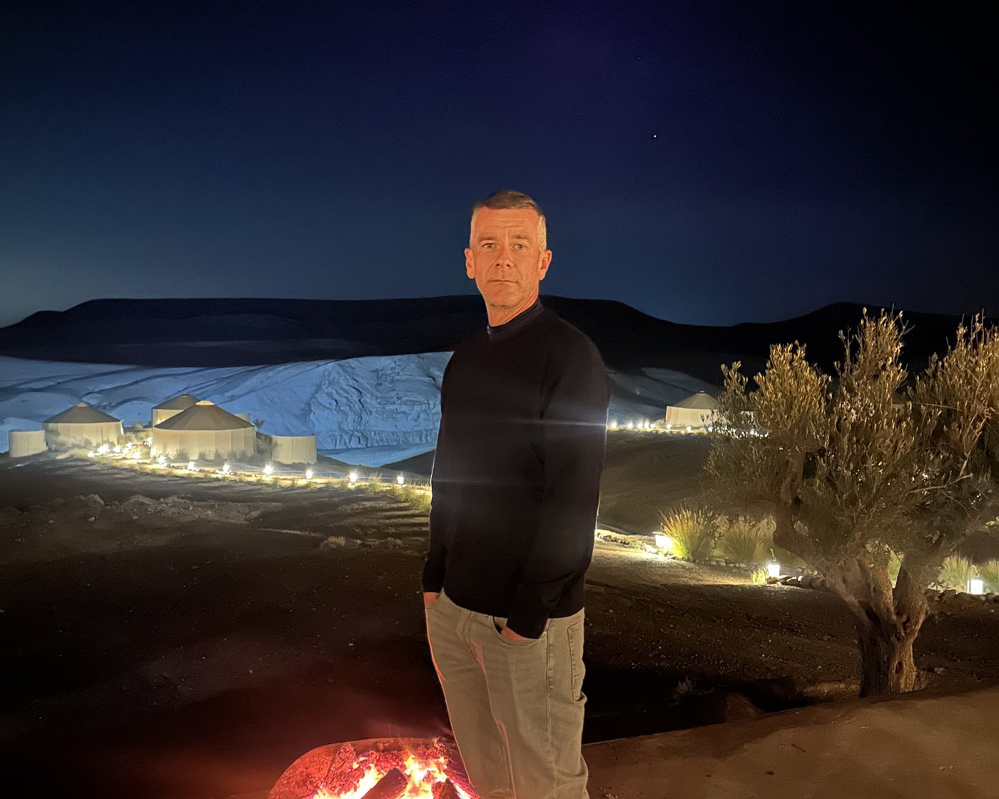 Carsten Diederich at dusk above a lit desert camp